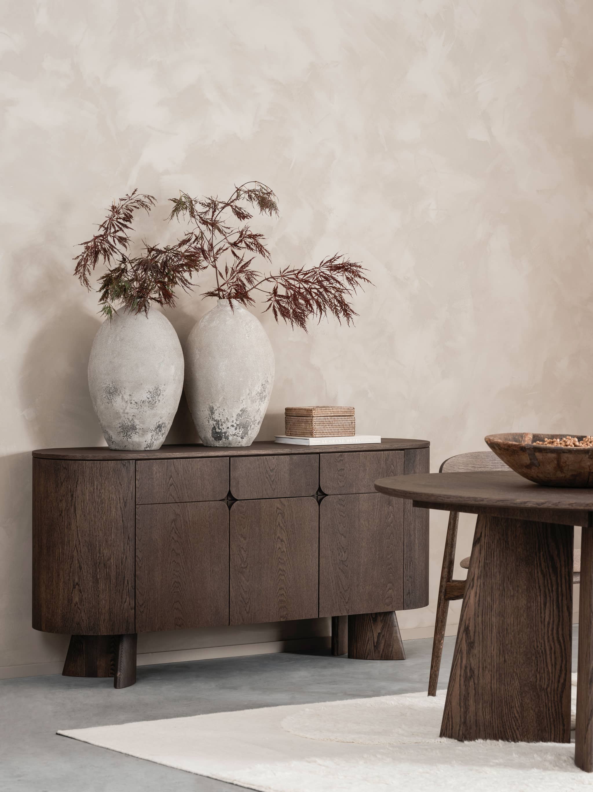 Elegant skjenk i Japandi-stil med mørkt treverk, i fargen mocca. Dekorert med to store vaser med naturlige grener. Minimalistisk interiørdesign med fokus på rene linjer og naturmaterialer
