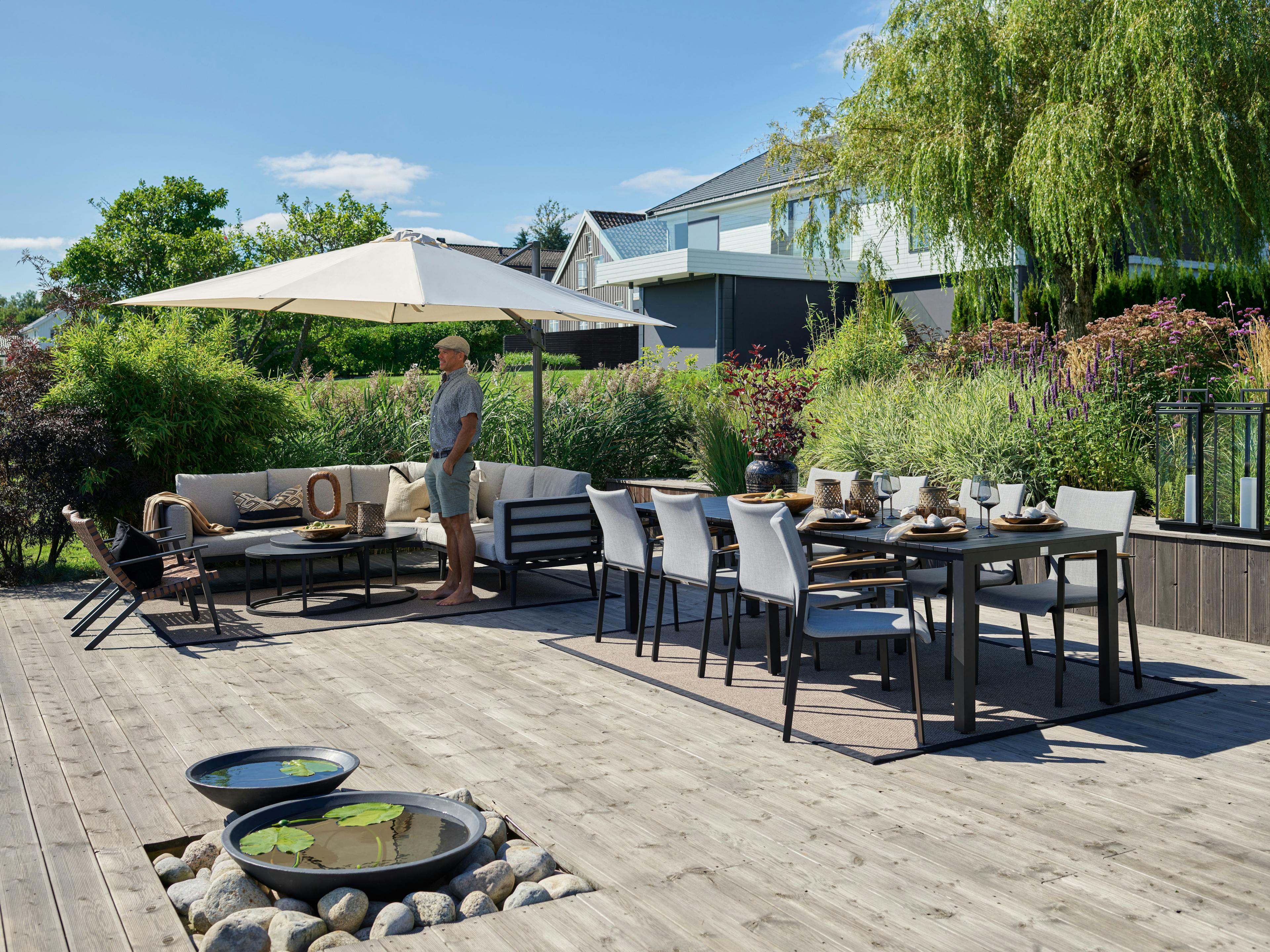 Hage med hagemøbler slik som hagesofa, utendørs spisebord, vannspeil og parasoll.